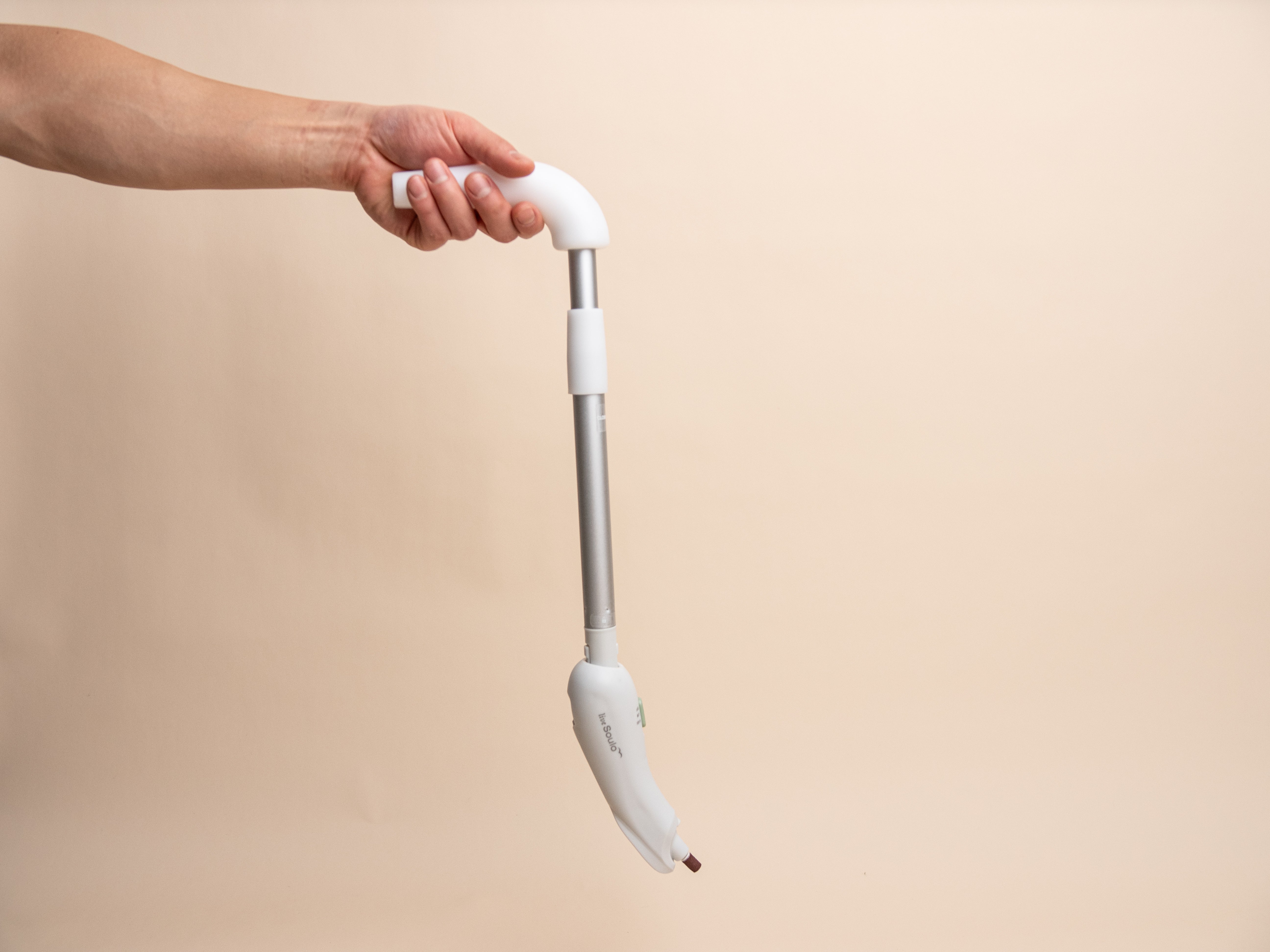 Hand holding a white long-handled nail filing device against a beige background