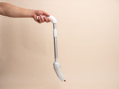 Hand holding a white long-handled nail filing device against a beige background