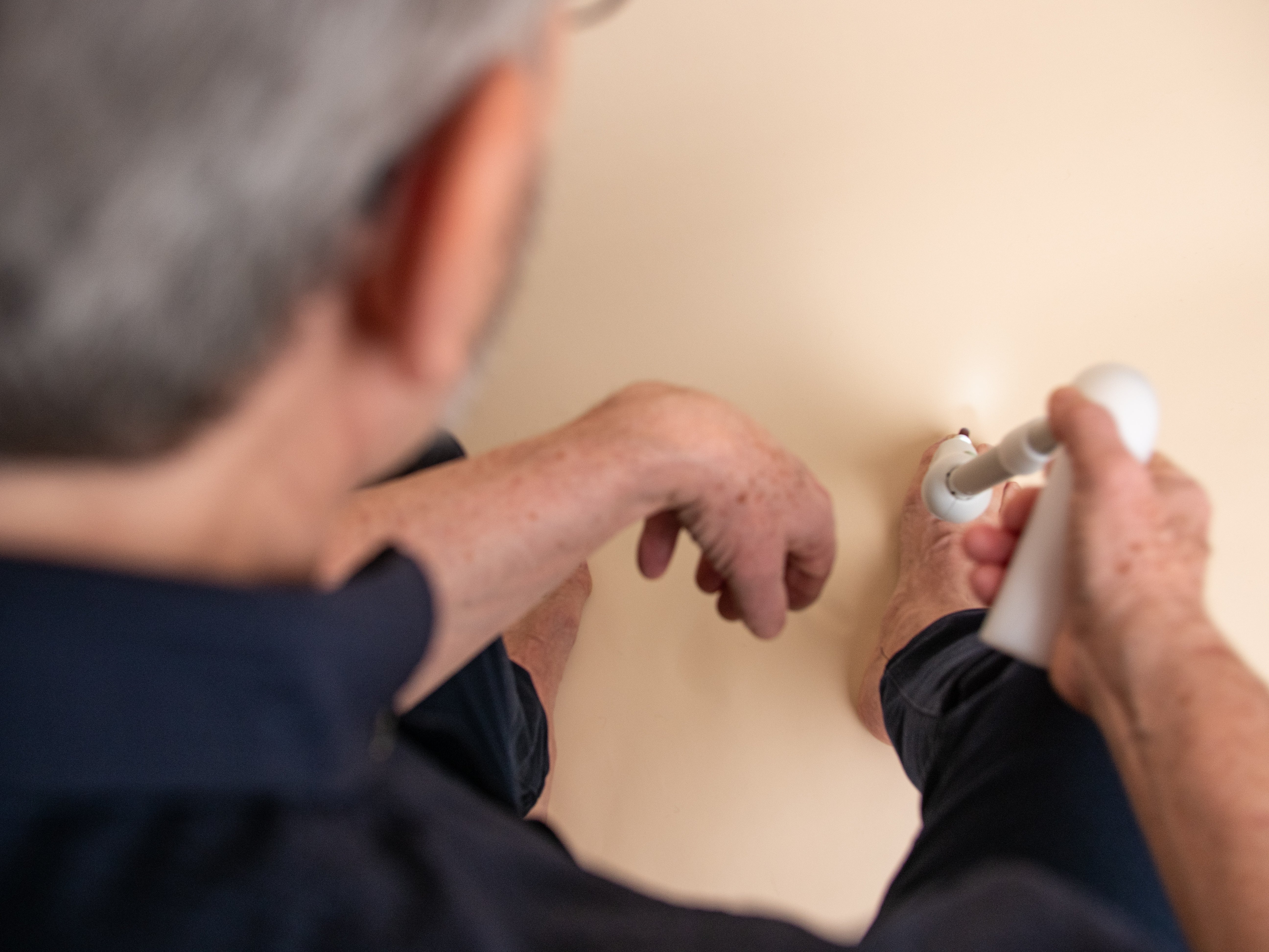 Person using a white long handled device to file down toenails on a beige colored floor