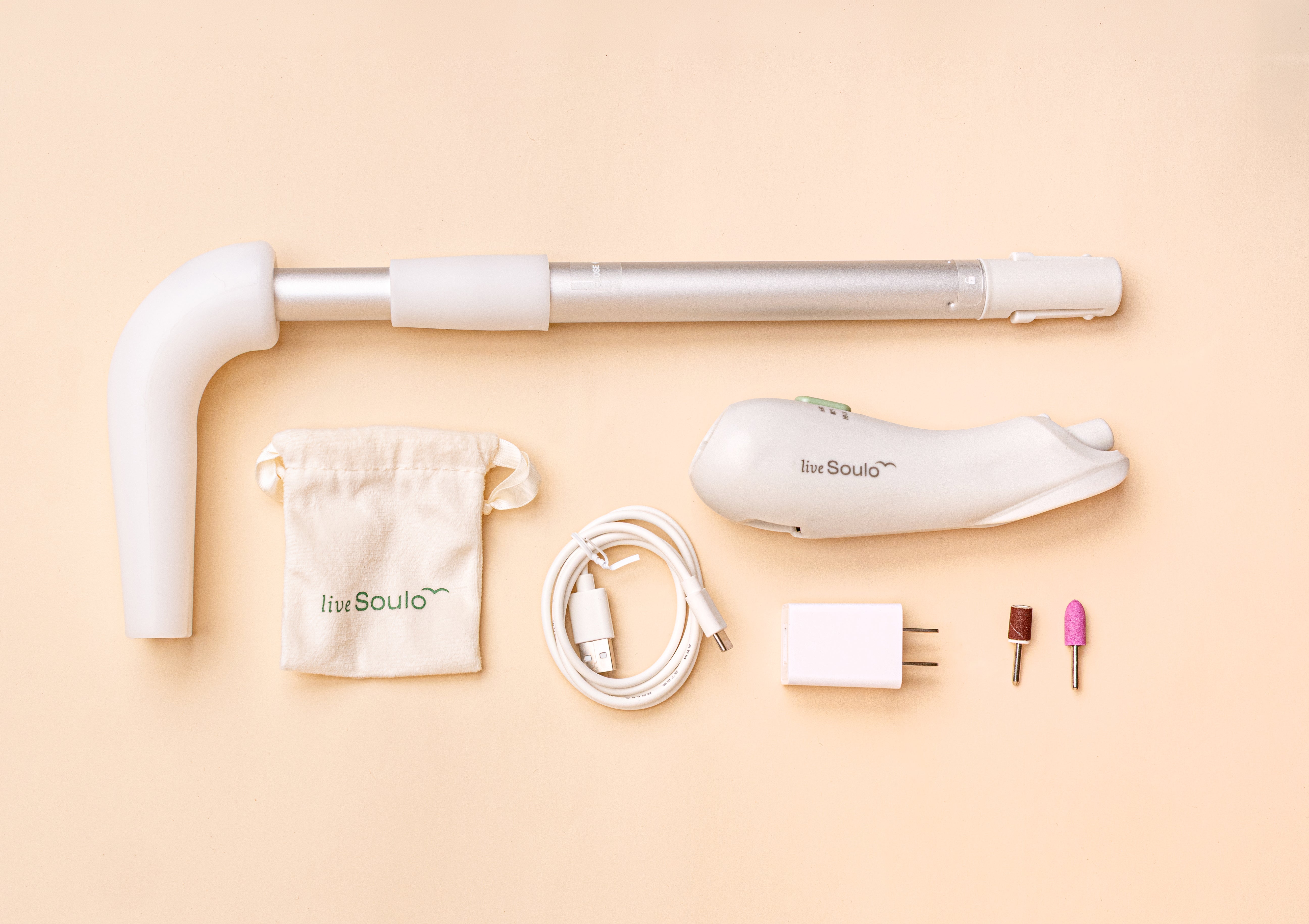Set of nail care tools including a white handheld device, cable, and accessories on a beige background.